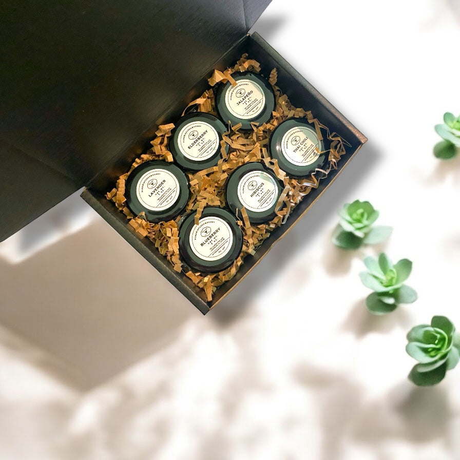 Six small glass infused raw honey jars with labels in a decorative box on a light surface with succulents.
