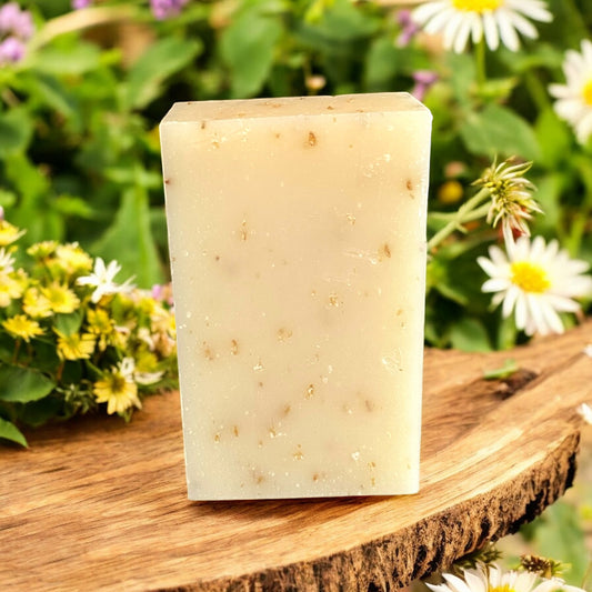 Bar of handcrafted soap on a wooden surface with flowers in the background