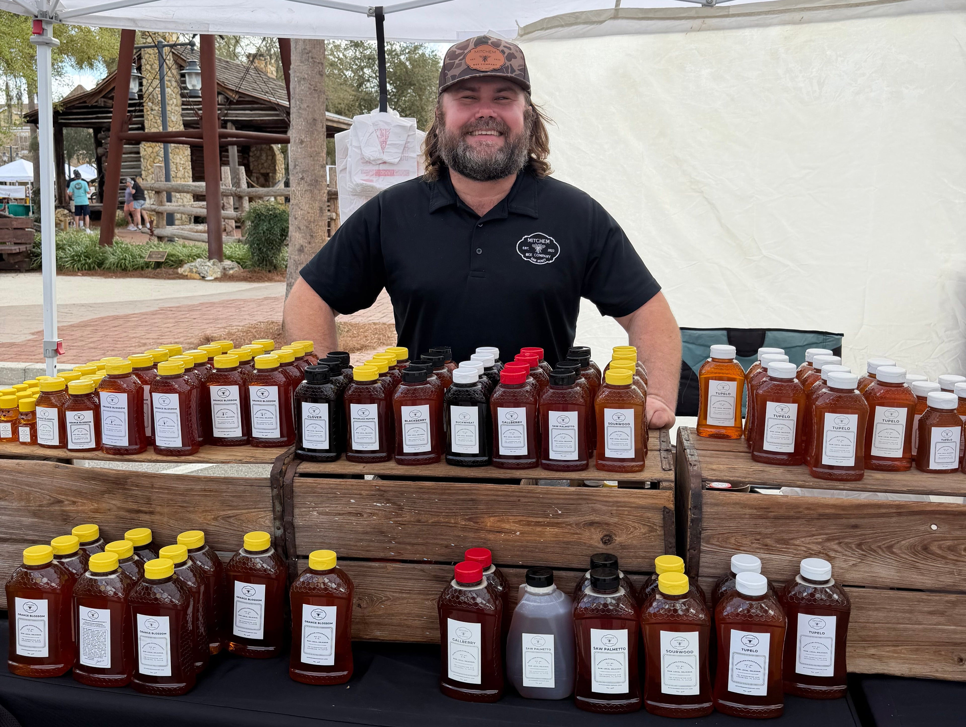Jake Mitchem standing behind his table at Brownwood Hometown Market in The Villages, FL with Mitchem Bee Company raw honey.