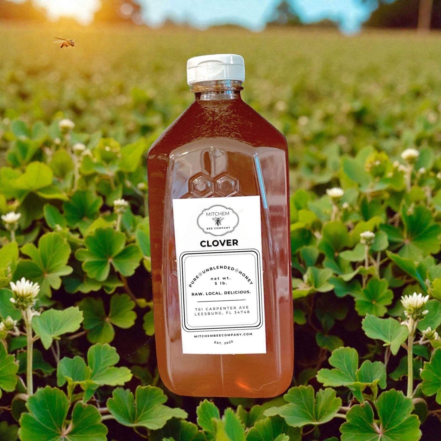 Bottle of clover honey with a label in a field of clover plants.