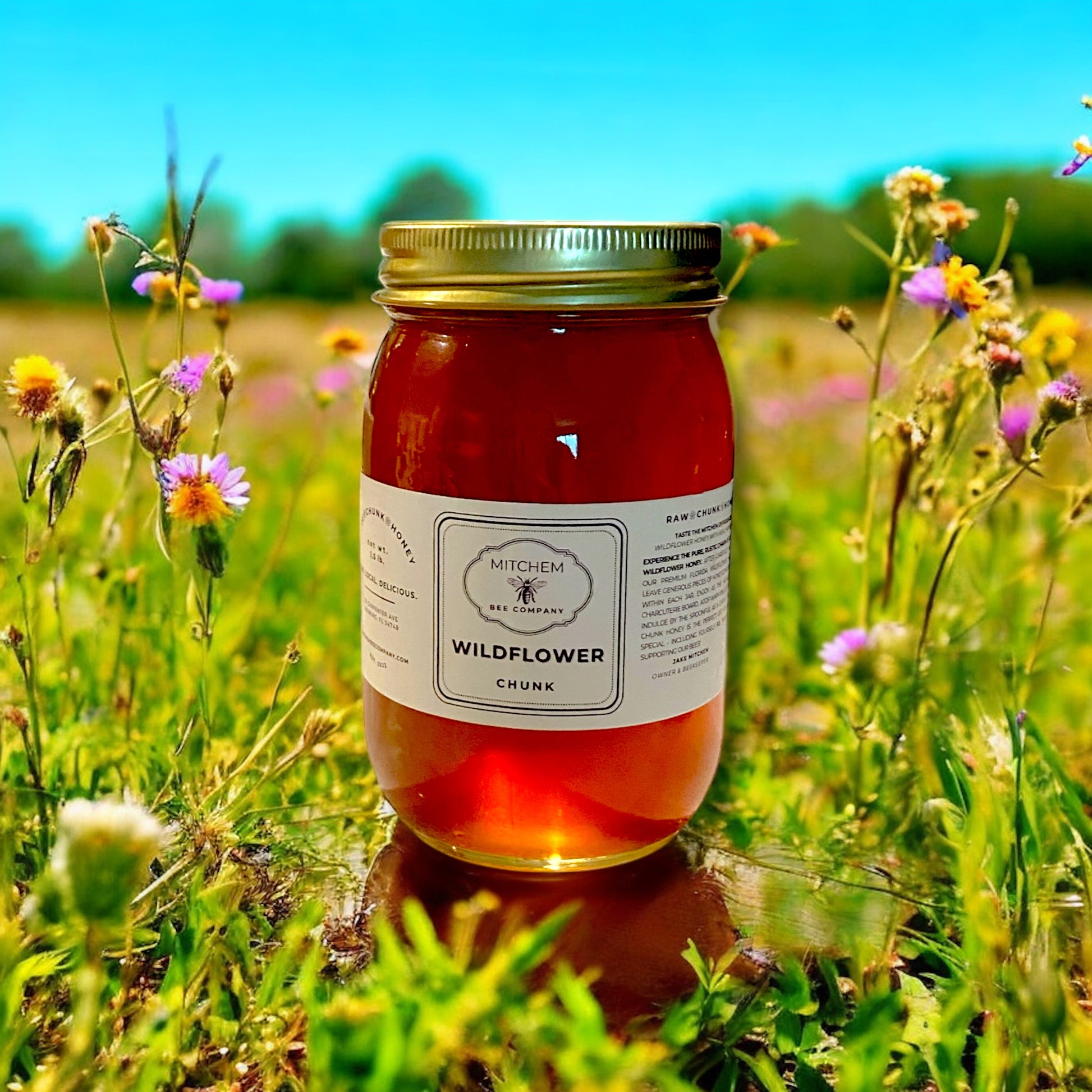 Jar of wildflower chunk honey in a field of flowers with a blue sky.