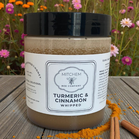 Jar of 'Turmeric & Cinnamon Whipped' by Mitchem Bee Company on a wooden surface with flowers in the background.