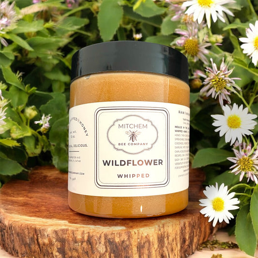 Jar of wildflower whipped honey from Mitchem Bee Company on a wooden surface with flowers in the background